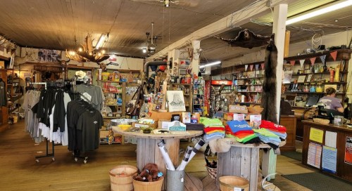 A cozy gift shop filled with clothing, souvenirs, and rustic decor, featuring wooden displays and a welcoming atmosphere.