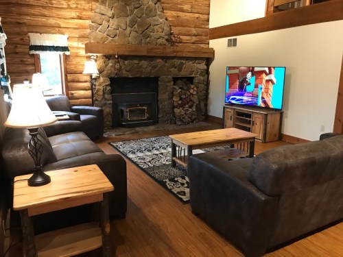 Cozy log cabin living room with a stone fireplace, two sofas, a wooden coffee table, and a TV.