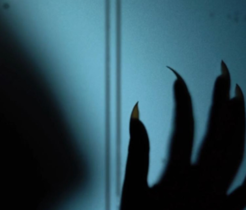 A shadowy hand with long, pointed nails reaches towards a light source, creating an eerie atmosphere.