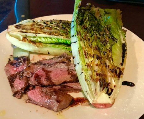 Grilled steak slices served with charred romaine lettuce on a white plate.