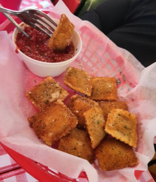 A basket of golden-brown fried ravioli served with a small bowl of marinara sauce for dipping.