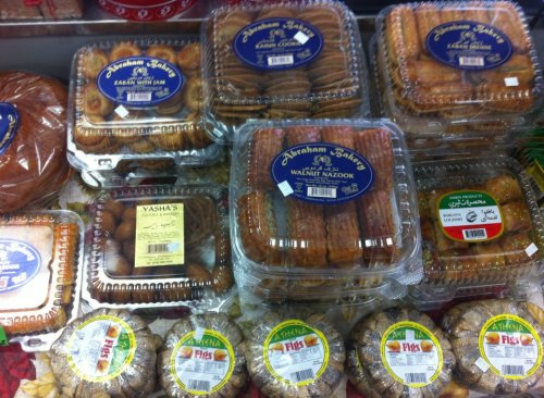 A variety of packaged pastries and sweets displayed in a bakery, featuring labels in Arabic and English.