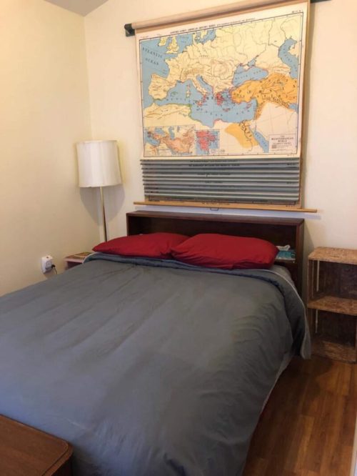 A cozy bedroom featuring a bed with red pillows, a wooden headboard, and a vintage map of Europe on the wall.
