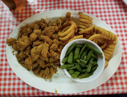 A plate of fried shrimp, curly fries, and green beans on a red-checkered tablecloth.