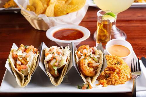 A plate with three tacos, rice, salsa, and a drink, accompanied by tortilla chips in a basket.