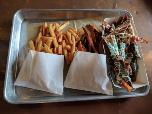 A metal tray with two servings of fries and a portion of loaded sweet potato fries topped with sauce.