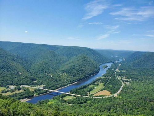 A scenic view of a winding river surrounded by lush green hills under a clear blue sky.