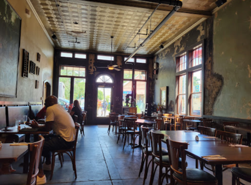 A spacious, rustic restaurant interior with wooden tables, chairs, and large windows letting in natural light.