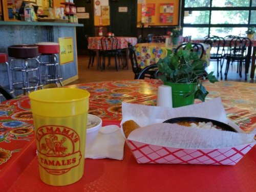 A colorful restaurant table with a yellow cup, a basket of tamales, and a side of rice in a cozy dining area.