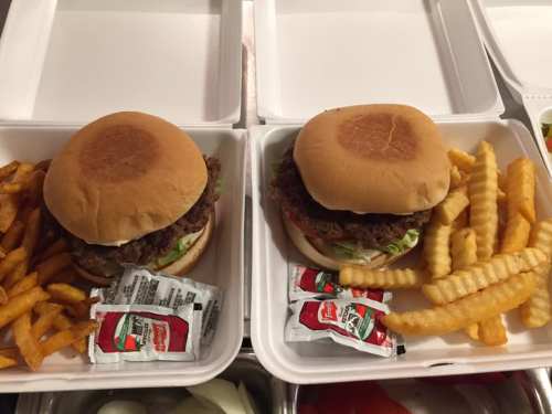Two burger boxes with sandwiches, lettuce, and ketchup packets, accompanied by crinkle-cut fries.