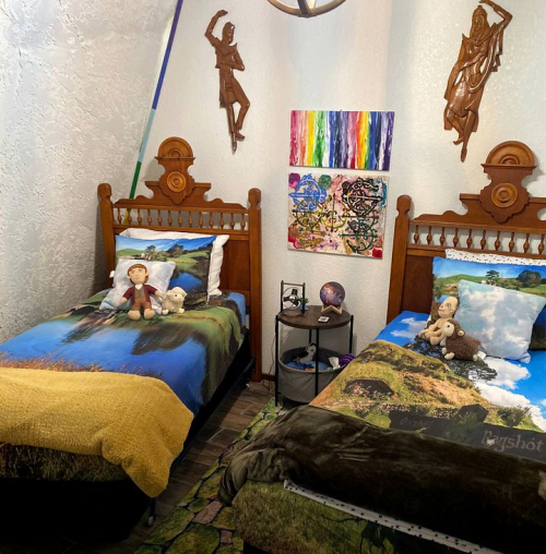 A cozy bedroom with two twin beds, colorful blankets, stuffed animals, and vibrant wall art.