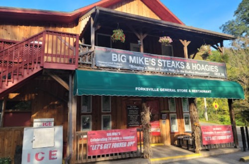 A rustic wooden building with a sign for Big Mike's Steaks & Hoagies, featuring banners and a green awning.