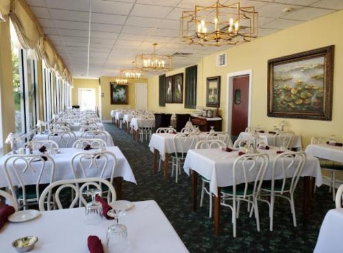 Brightly lit restaurant interior with white tablecloths, elegant chandeliers, and large windows overlooking greenery.