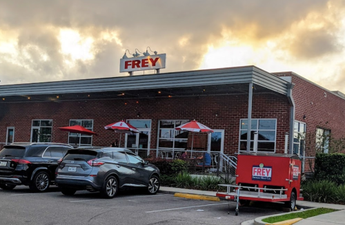 Exterior of a restaurant named "Frey," featuring outdoor seating and a food truck, under a cloudy sky.
