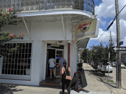 A woman enters Loretta's restaurant, with a sign and street view in a sunny neighborhood.