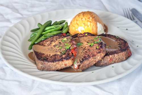 A plate featuring two slices of meatloaf with gravy, green beans, and a scoop of mashed potatoes.