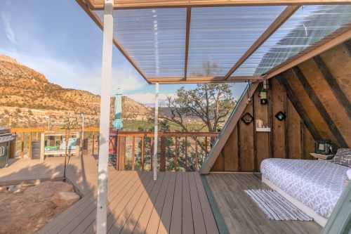 Cozy outdoor deck with a bed, overlooking a scenic landscape of mountains and trees.
