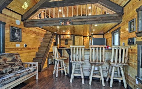Cozy wooden interior of a tiny home featuring a bar, seating area, and a staircase leading to a loft.