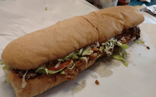 A long sandwich filled with shredded lettuce, tomatoes, and meat, served on a soft hoagie roll.