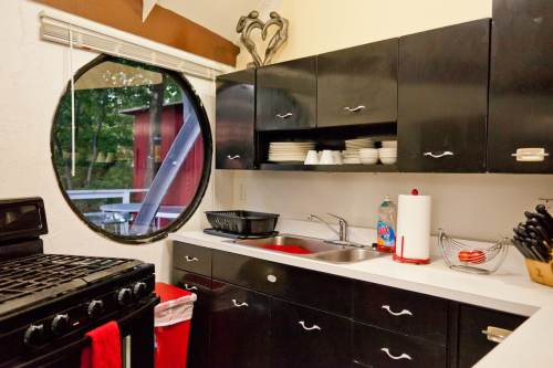 A modern kitchen with black cabinets, a round window, and a stove, featuring dishes and utensils neatly arranged.