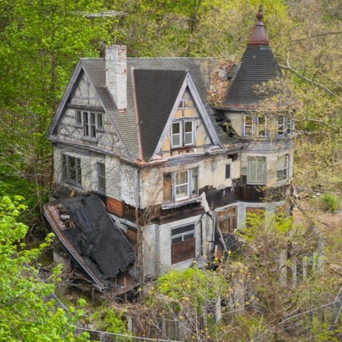 An abandoned, dilapidated house surrounded by overgrown trees and vegetation, showcasing signs of decay and neglect.