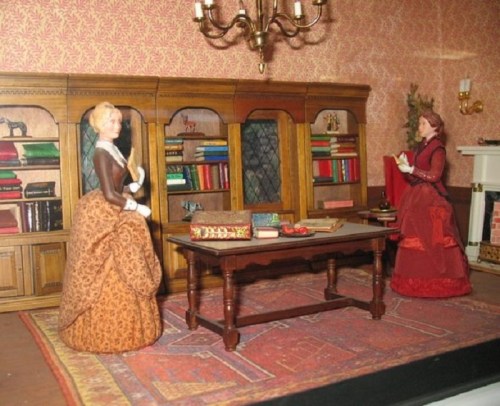 Two dolls in a vintage-style room with bookshelves, a table, and ornate decor, dressed in 19th-century attire.