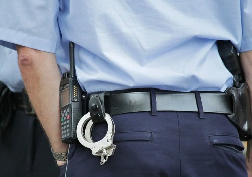 A close-up of a police officer's waist, featuring a radio and handcuffs attached to a belt.