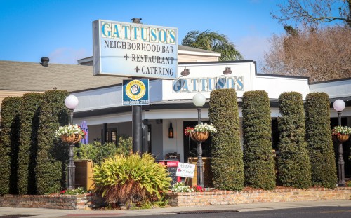 Exterior of Gattuso's Neighborhood Bar and Restaurant, featuring greenery and a sign, on a sunny day.
