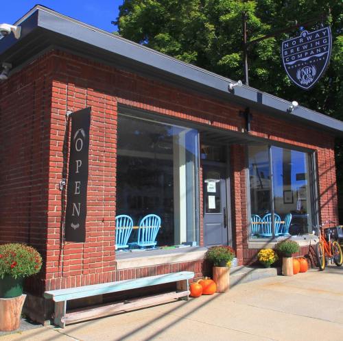 A brick building with large windows, an "Open" sign, and blue chairs outside, surrounded by pumpkins and bicycles.