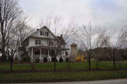 A large white house with a porch, surrounded by bare trees and a grassy lawn, under a cloudy sky.