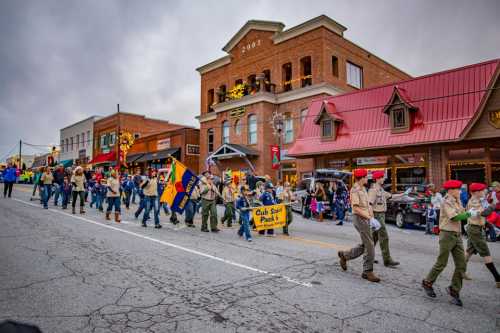 A parade with participants in uniforms marching down a street, featuring buildings decorated for the season.