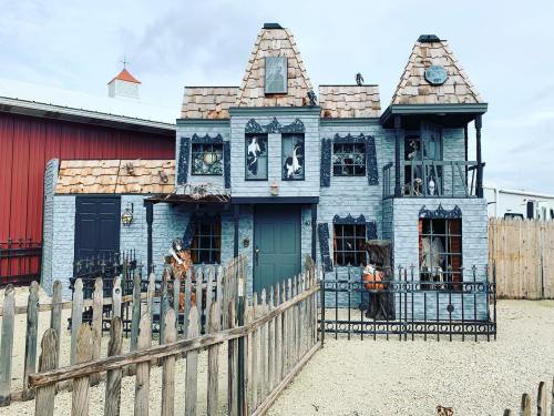 A spooky, blue-painted house with a unique roof, surrounded by a wooden fence and eerie decorations.