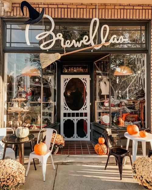 Charming storefront decorated for fall, featuring pumpkins, a broom, and a whimsical sign reading "Brewella's."