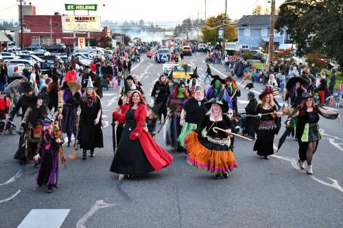 A lively parade of people in costumes, including witches, walking down a street with spectators on both sides.