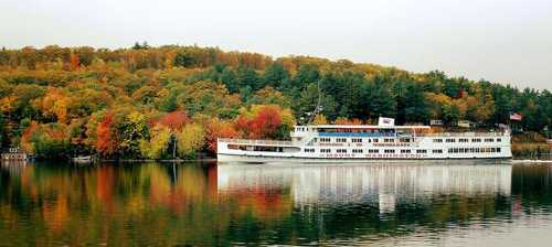 A white boat on a calm lake, surrounded by vibrant autumn foliage reflecting in the water.