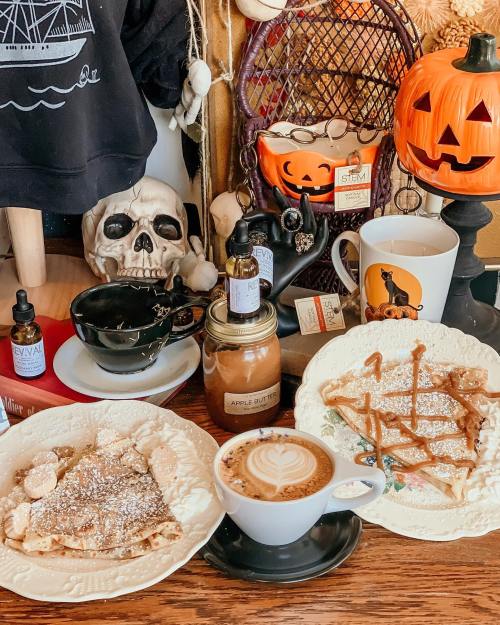 A cozy table setting with pancakes, coffee, and decorative Halloween items, including a pumpkin and a skull.