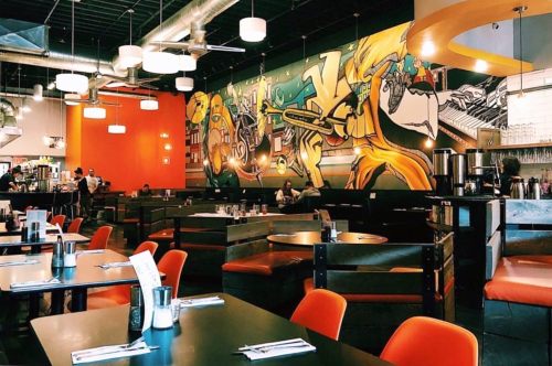 A modern restaurant interior featuring vibrant murals, orange accents, and empty tables ready for diners.