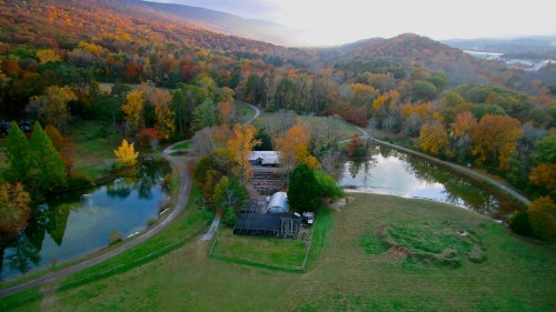 Aerial view of a scenic landscape with autumn foliage, a farm, ponds, and rolling hills in the background.