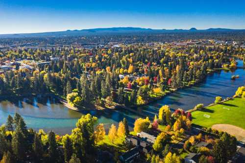 Aerial view of a vibrant landscape with rivers, trees in autumn colors, and a town in the background under a clear blue sky.