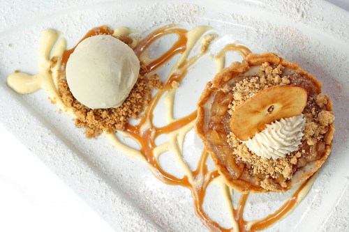 A dessert plate featuring an apple tart with whipped cream, caramel drizzle, and a scoop of ice cream on the side.