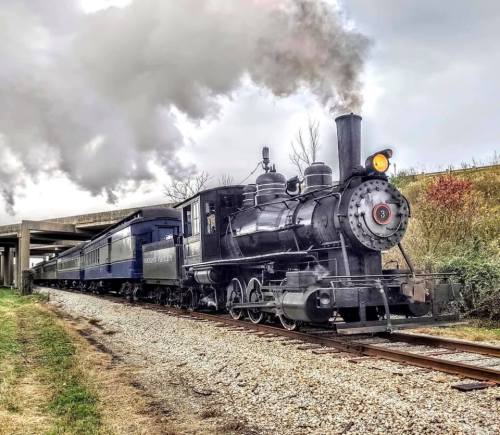 A vintage steam locomotive with a black engine and blue passenger cars, emitting smoke, on a gravel track.