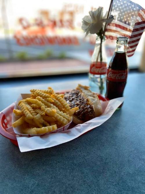 A plate with crinkle-cut fries and a hot dog, alongside a Coca-Cola and a small vase with a flower and an American flag.