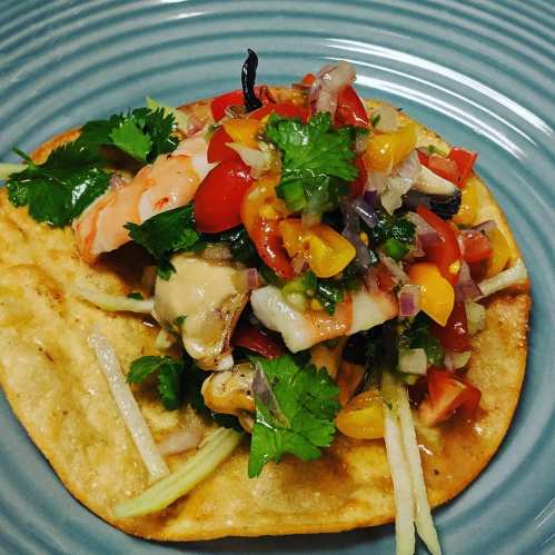 A colorful taco topped with shrimp, fresh vegetables, and herbs on a blue plate.