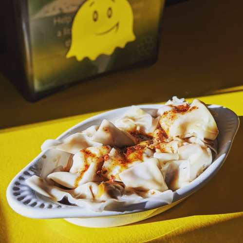 A white dish filled with dumplings topped with a sprinkle of spices, set against a bright yellow background.