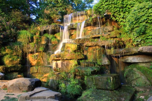 A serene waterfall cascading over moss-covered rocks, surrounded by lush greenery.