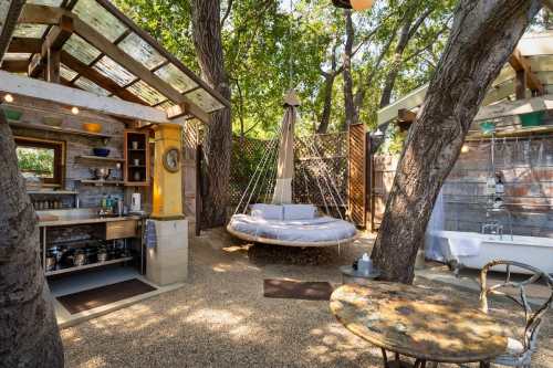 A cozy outdoor space featuring a swing, kitchenette, and rustic decor surrounded by trees.