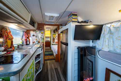 Cozy interior of a camper van featuring a kitchen, living area, and bedroom with colorful decor and natural light.