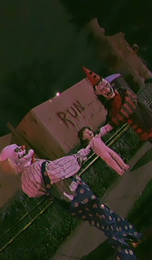 Two creepy clowns hold a child in a dark, eerie setting with a "RUN" sign in the background.
