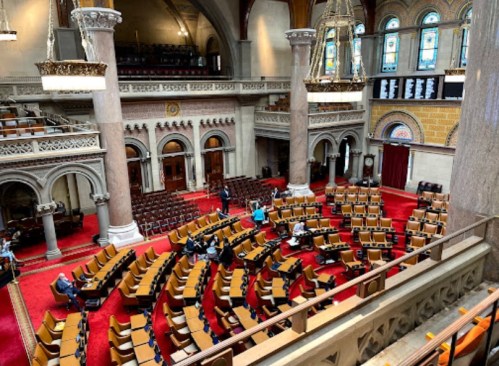 A wide view of a legislative chamber with rows of empty seats and ornate architecture.