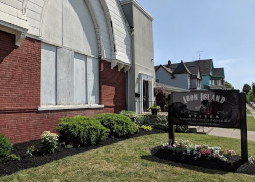A brick building with a sign reading "Iron Island" and a landscaped garden in front.